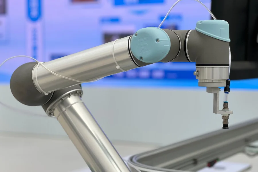 Un robot colaborativo plateado y azul claro con una pequeña herramienta de vacío sobre una superficie de trabajo.